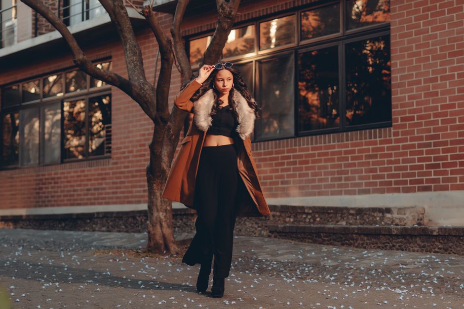 Elegant woman posing outdoors in stylish coat and sunglasses.