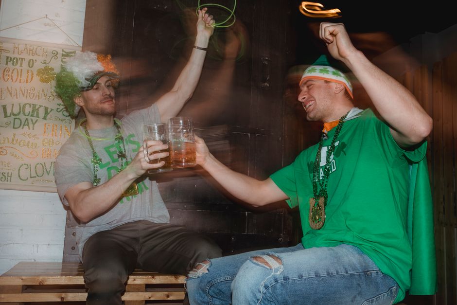 Cheerful young friends in national color clothes and wig drinking beer celebrating national holiday
