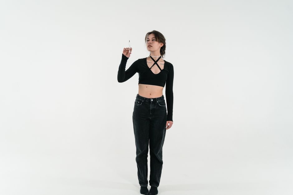 A young woman in a stylish black outfit holds a syringe, standing against a white background.