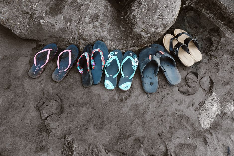A collection of vibrant flip flops left on the sand in Bali, Indonesia, depicting a casual beach vibe.