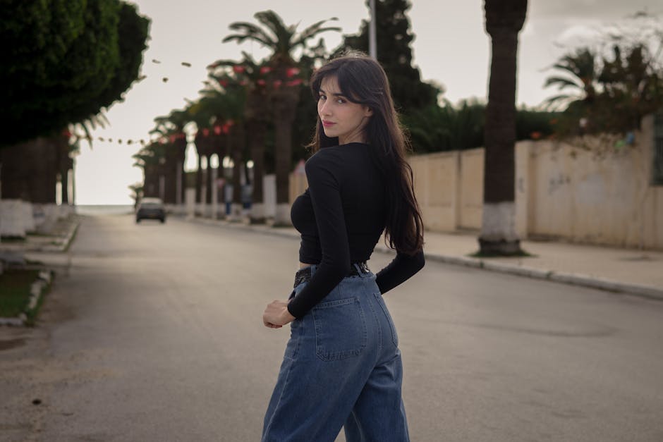 Woman posing confidently on an urban palm-lined street at daylight.
