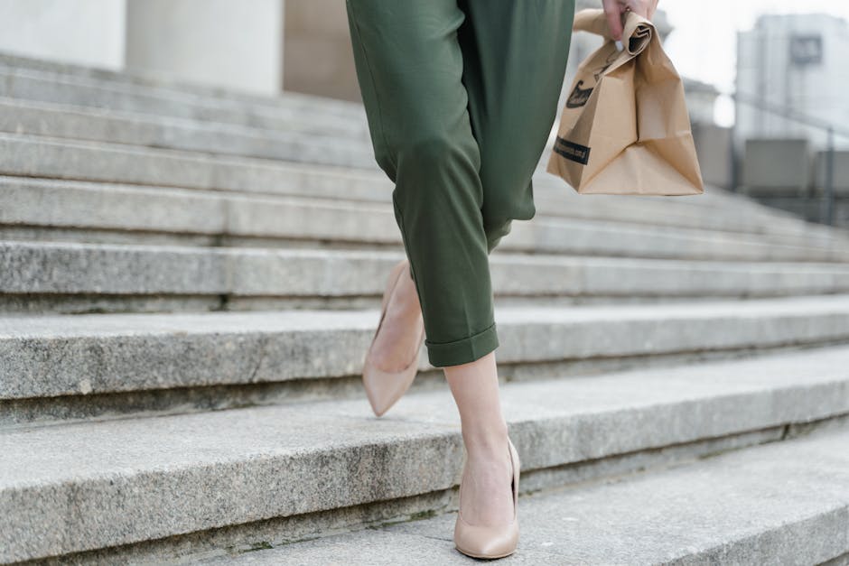Fashionable woman in high heels descends stairs holding a paper bag, highlighting urban style.