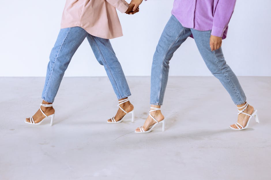 Two women walking stylishly in high heels and jeans against a white background.