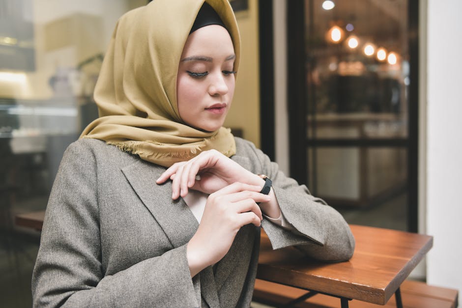 A young woman in a beige hijab looking at her smartwatch indoors.