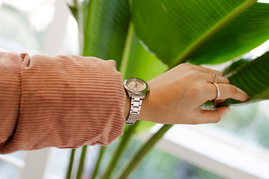 A close-up of a hand with a silver watch touching a banana leaf, showcasing brown long sleeves.