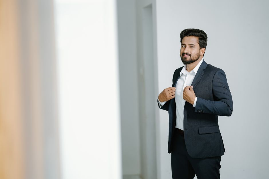 A confident man in a gray suit standing indoors, showcasing fashion and style.