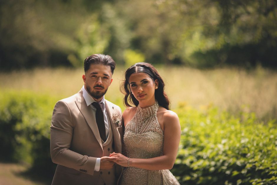 A stylish couple posing for a wedding portrait in a lush outdoor setting.