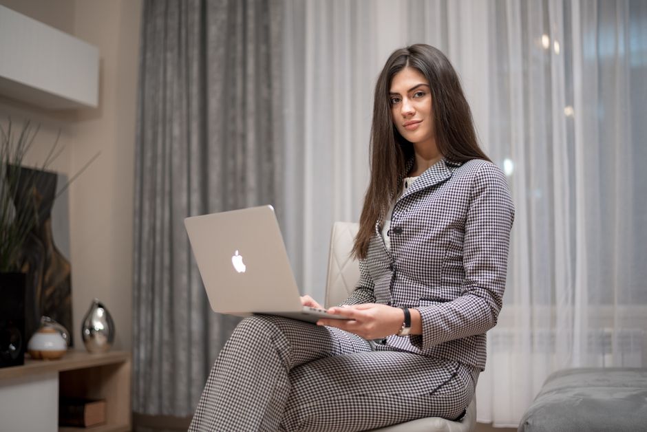 Confident woman using a laptop at home for remote work in a stylish living room.