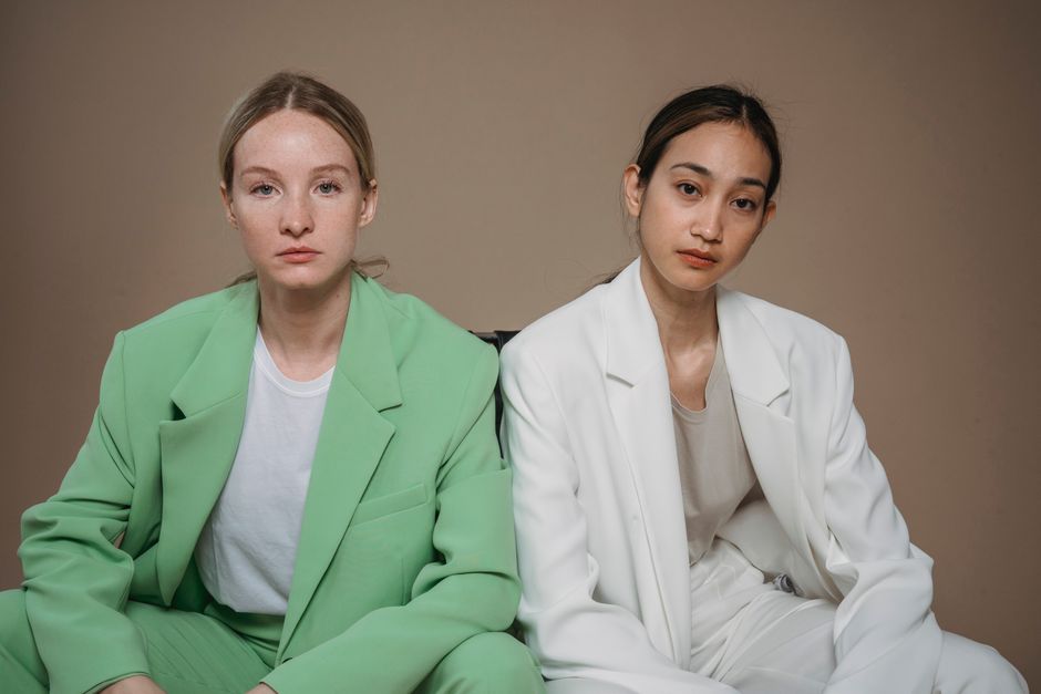 Portrait of two women in green and white suits sitting on a beige background.