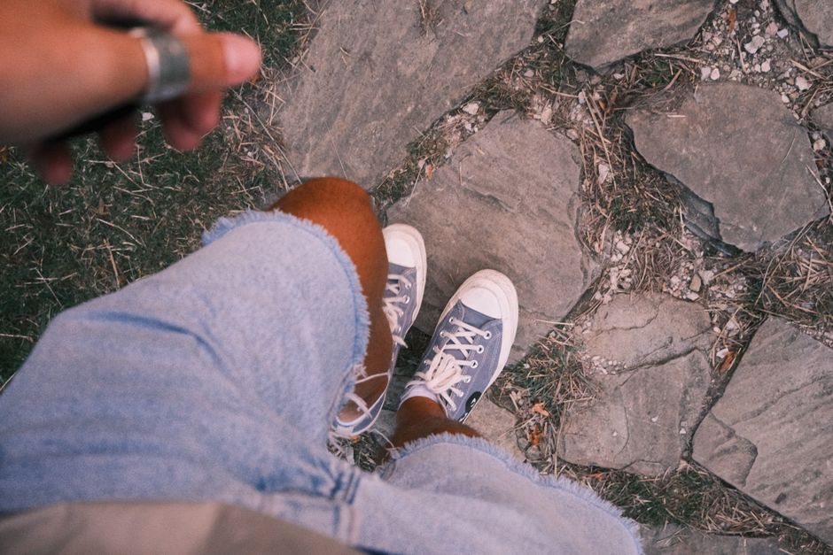 Top view of a person in sneakers and shorts standing on a stone pathway outdoors.