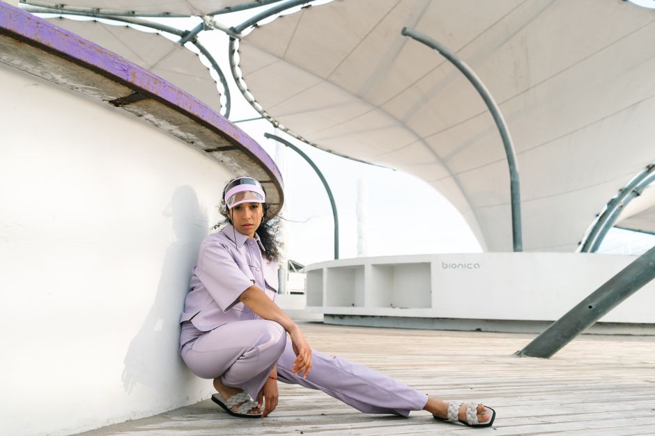 A stylish woman in a lavender outfit poses at a modern outdoor structure, expressing urban fashion and individuality.