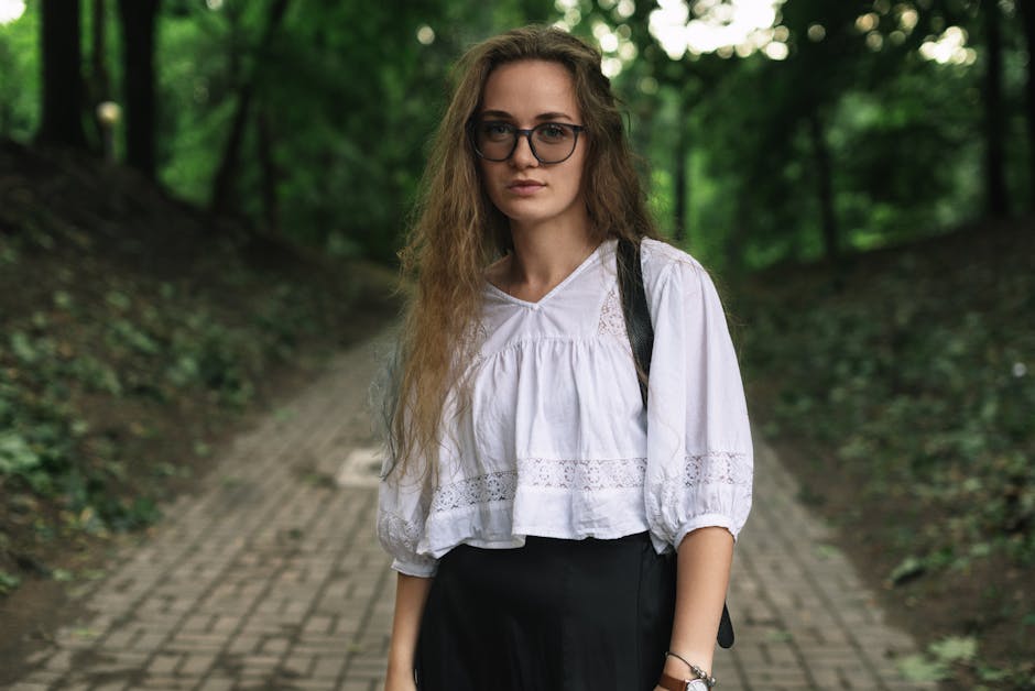 Portrait of a young woman with glasses in a park, wearing white blouse.