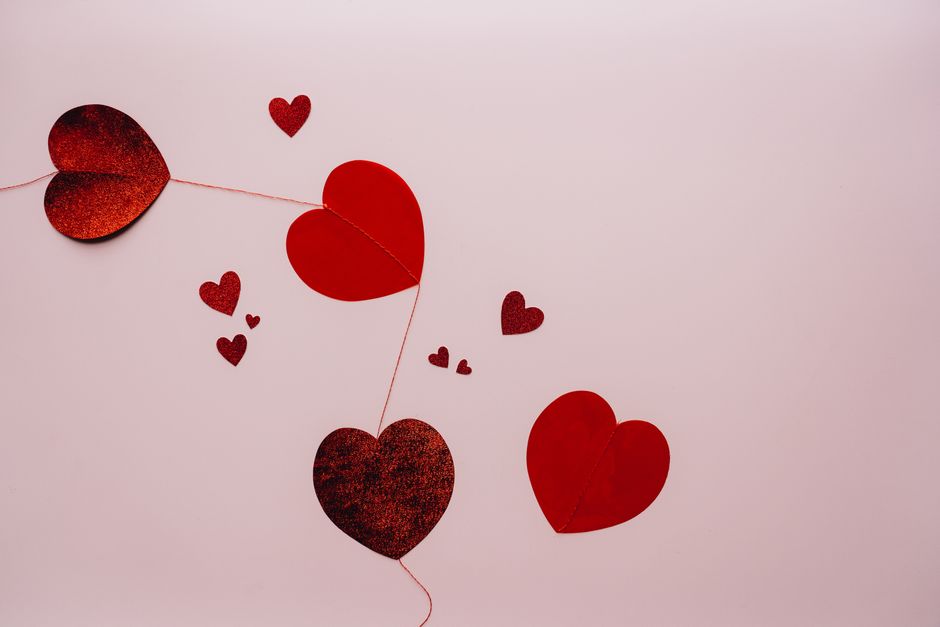 A collection of red hearts on a string against a soft pink background, perfect for romantic and Valentine's Day themes.