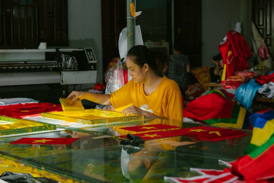 A woman screen prints flags at a vibrant textile workshop indoors.