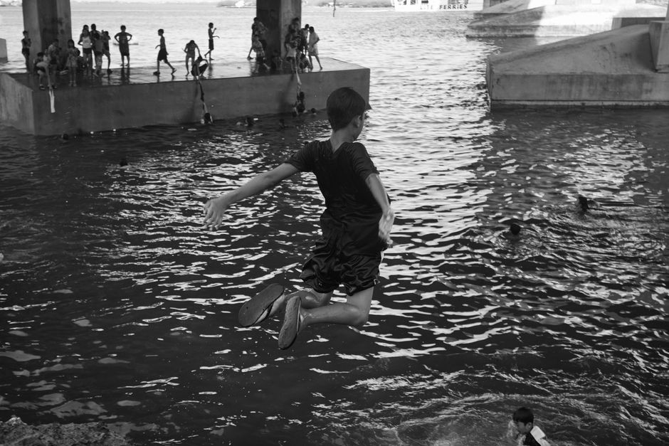 A young boy jumps into a river under a bridge, highlighting carefree summer fun.