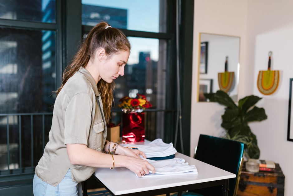 A woman folding clothes at a table in a bright, modern home office setting.
