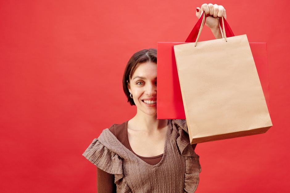 Joyful woman holding shopping bags against a bright red backdrop, expressing excitement.