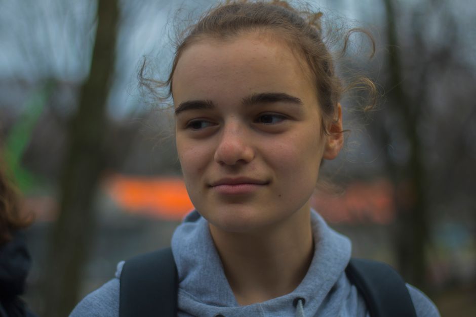 A young woman in a hoodie smiles softly outdoors, capturing an autumn day.
