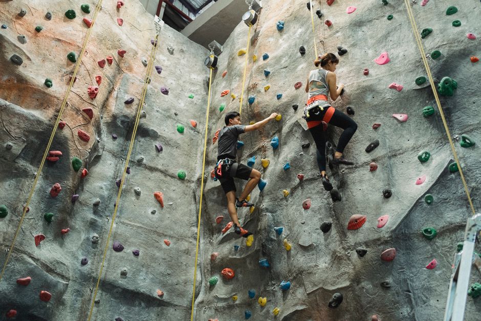 Low angle of strong woman exercising with male friend on climbing wall in gym