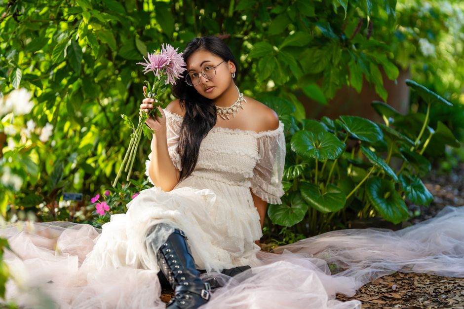 Elegant woman in white dress in a lush garden, holding flowers and embodying serenity.