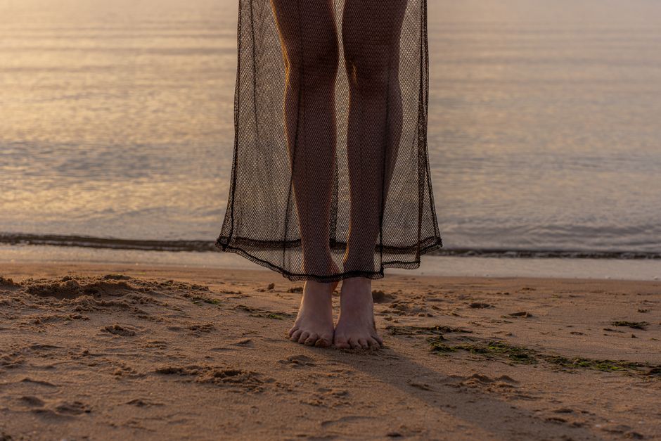 Close-up of bare feet on a sandy beach during sunset, capturing serene coastal vibes.