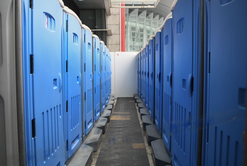 A series of blue portable toilets aligned at an outdoor construction site.