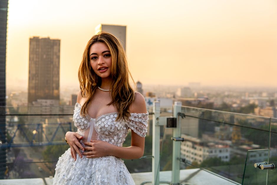 Young woman in a white dress on a rooftop in Mexico City during sunset, with a vibrant cityscape backdrop.