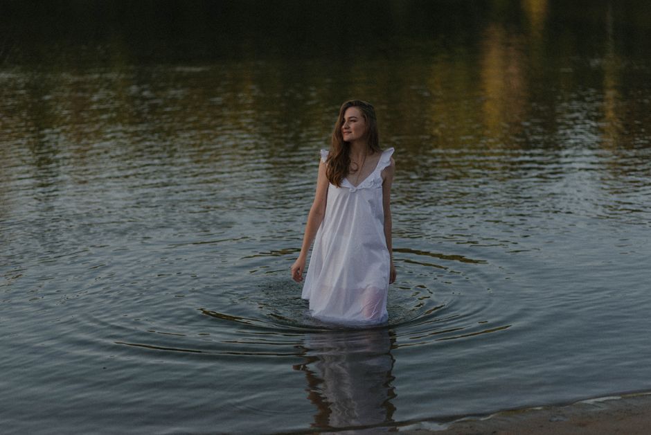 A serene moment captured of a woman wading through a tranquil lake at sunset.