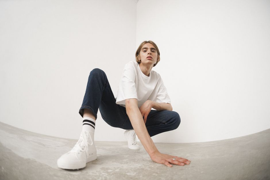 Crouching model in denim and white shirt, stylish minimalist studio shoot.