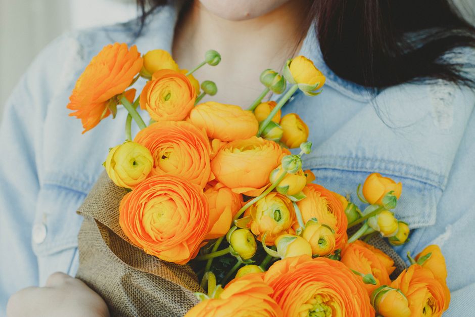 Crop faceless female in denim jacket holding beautiful bouquet of yellow Ranunculus flowers