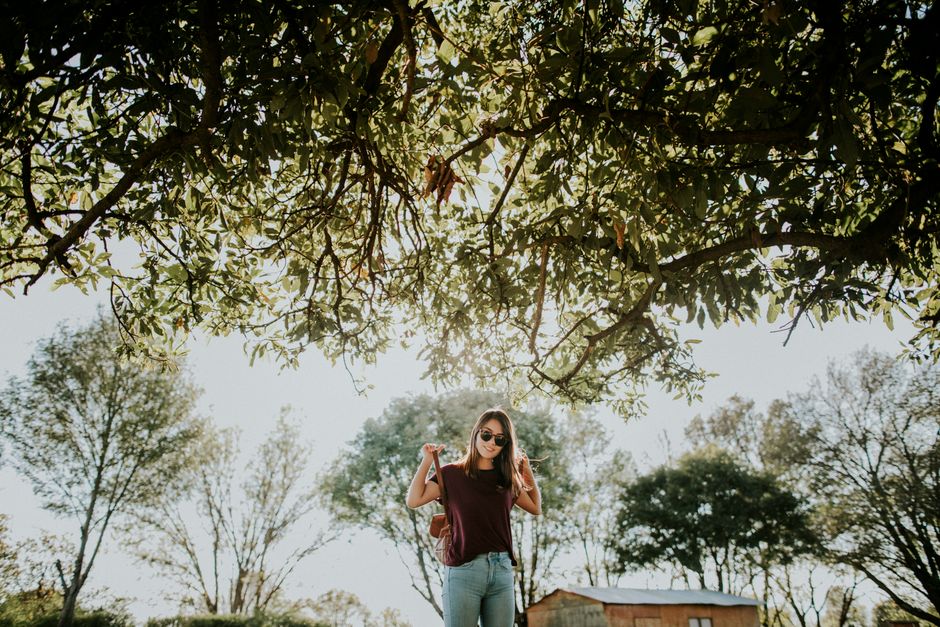 Casual young woman in sunglasses enjoying a sunny day under a tree canopy.