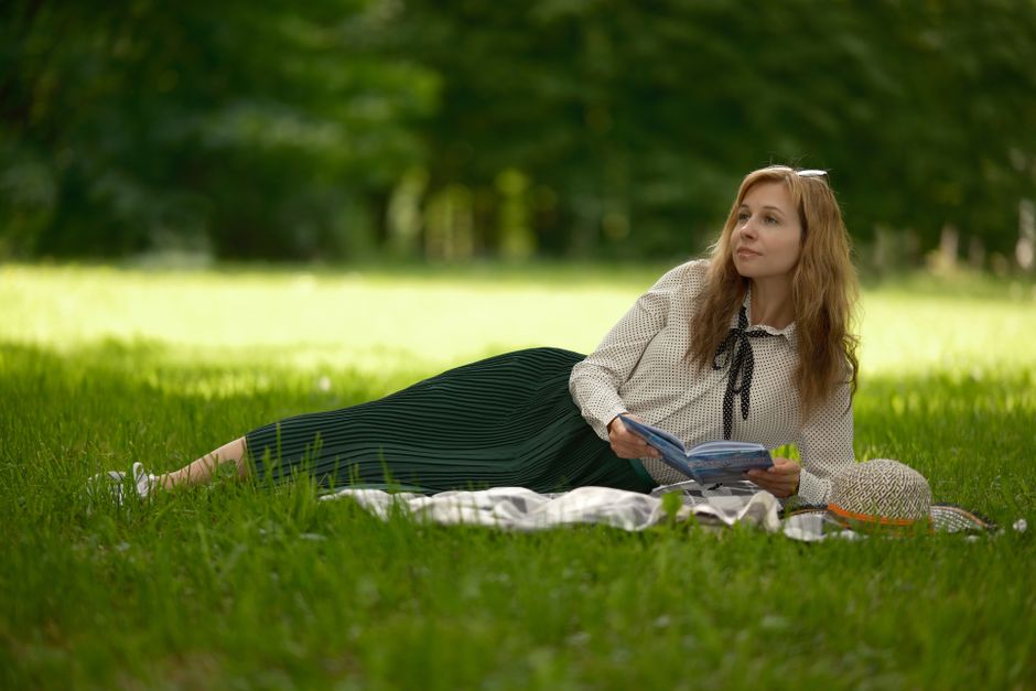 A woman leisurely reading a book while lying on grass in a park, enjoying a sunny day.