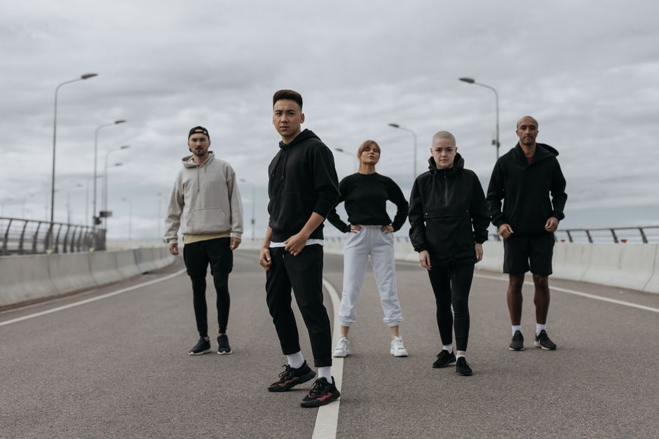Five diverse friends in sportswear posing confidently on an empty urban road.