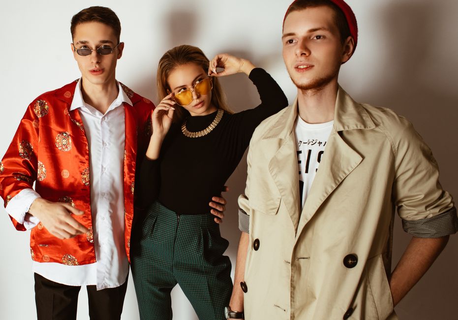 Fashionable portrait of three adults showcasing trendy outfits and accessories indoors.