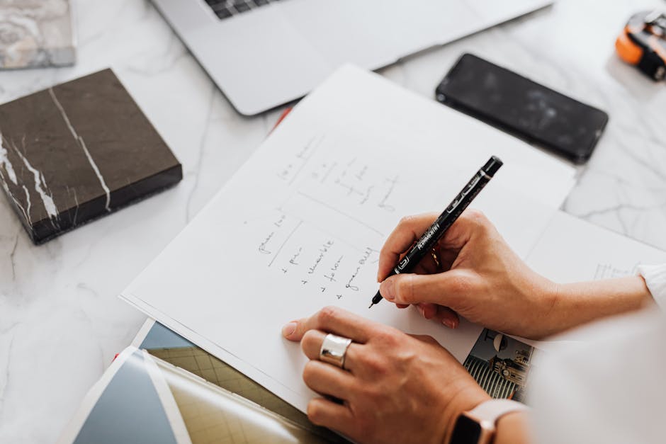 Hands writing ideas in a notebook, symbolizing creativity and productivity in an office setting.