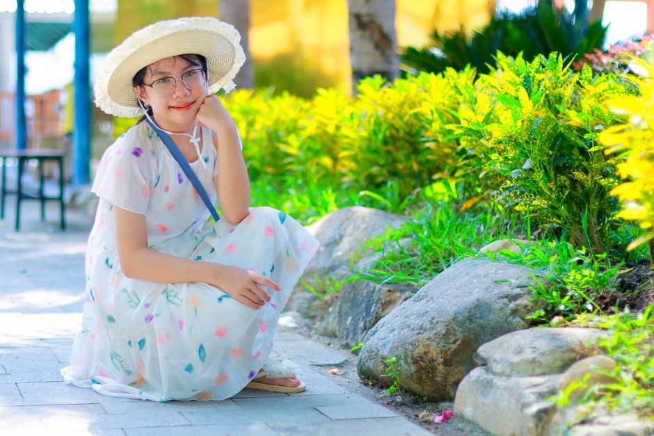 Woman in a floral dress and sun hat enjoying a sunny day in a garden setting.