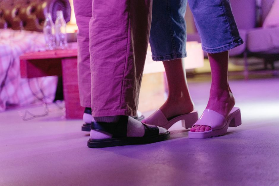 Casual close-up of a couple's feet indoors with purple lighting and stylish footwear.