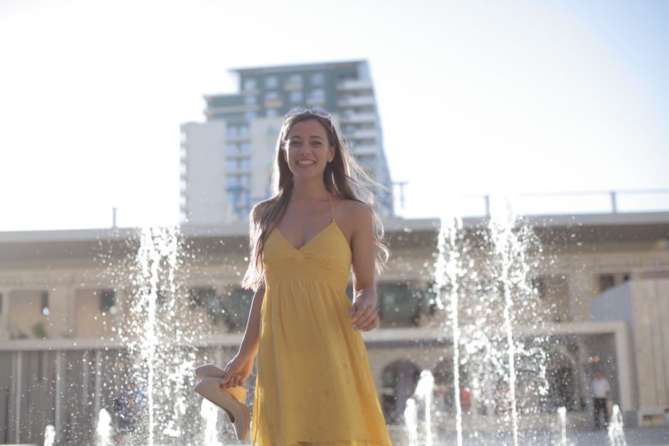 Smiling woman in a yellow dress enjoying a sunny day by a fountain.