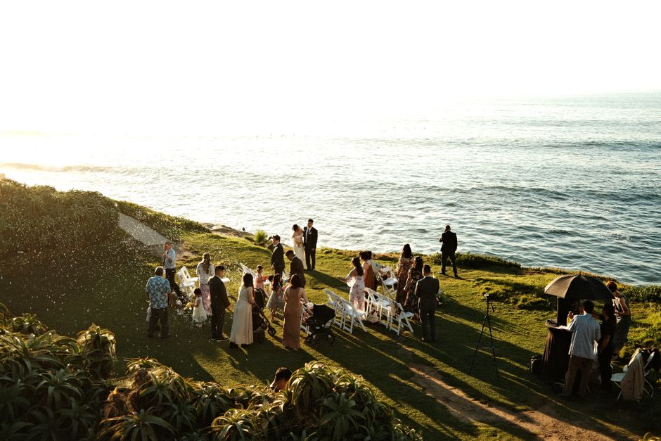 Elegant seaside wedding ceremony with guests gathered on a cliffside during sunset.