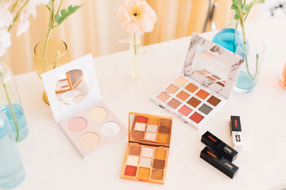 Aesthetic display of makeup palettes and lipsticks surrounded by flowers.