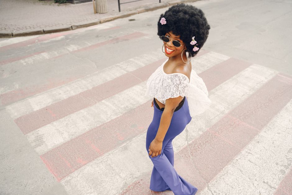 Fashionable woman in sunglasses and floral afro hair walking confidently on a crosswalk, exuding style and joy.