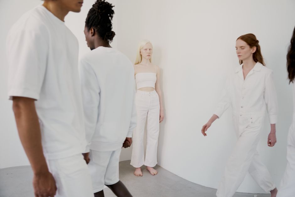 People in white clothing posing artistically against a white background, showcasing modern diversity.