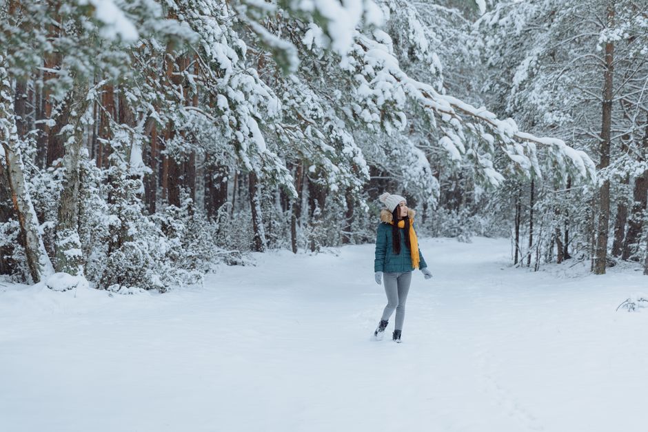 A woman walks through a serene snowy forest, embracing the winter atmosphere.