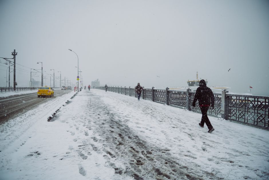 A winter street scene with snow, a yellow taxi, and pedestrians on a snowy urban bridge.