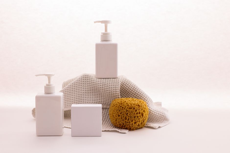 White pump bottles with a natural sponge on a textured cloth, ideal for beauty product mockups.