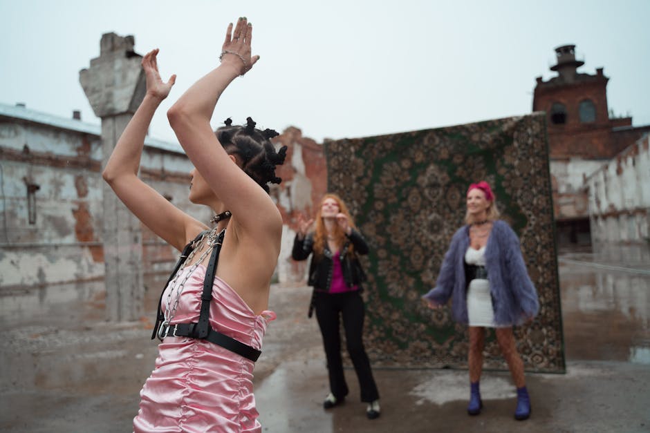 Three stylish women pose with raised arms in an urban outdoor setting with a vibrant carpet backdrop.