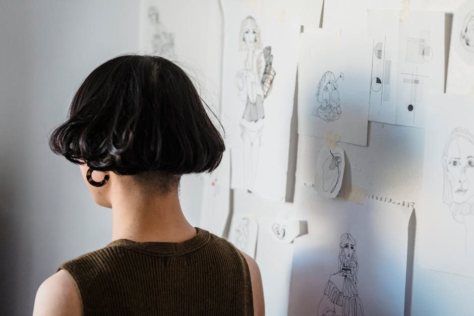 A woman with short dark hair examines sketches displayed on a wall, focusing on creativity.